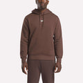 A man wearing the Reebok Men's Finisher Hoodie with a front pocket and matching brown pants stands against a plain white background.