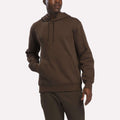 A man wearing the Reebok Men’s Finisher Hoodie, featuring a front pocket, along with matching brown pants stands against a plain white background.