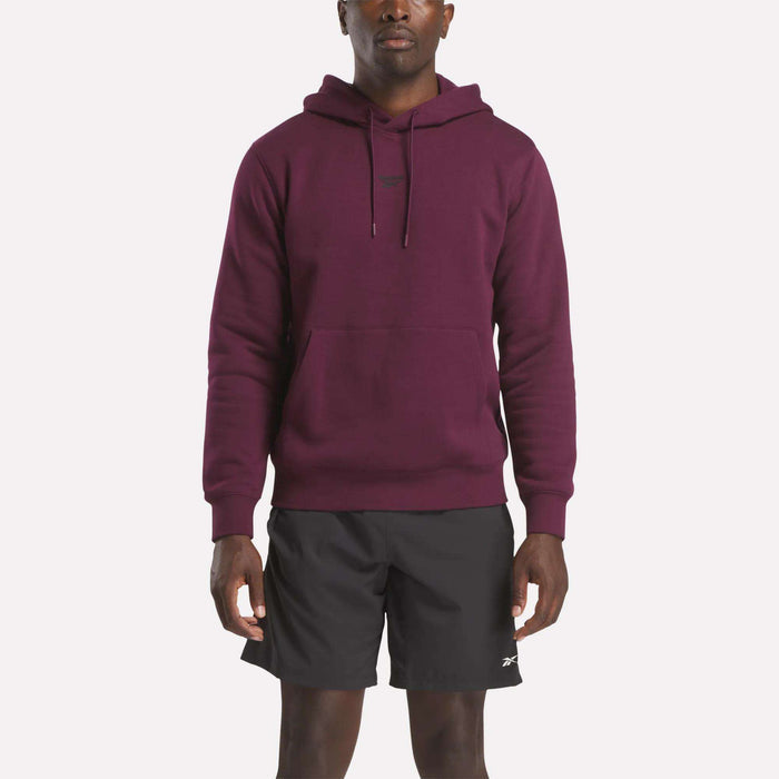A person wearing a maroon Reebok Men's Finisher Hoodie and black athletic shorts stands facing forward against a plain white background.