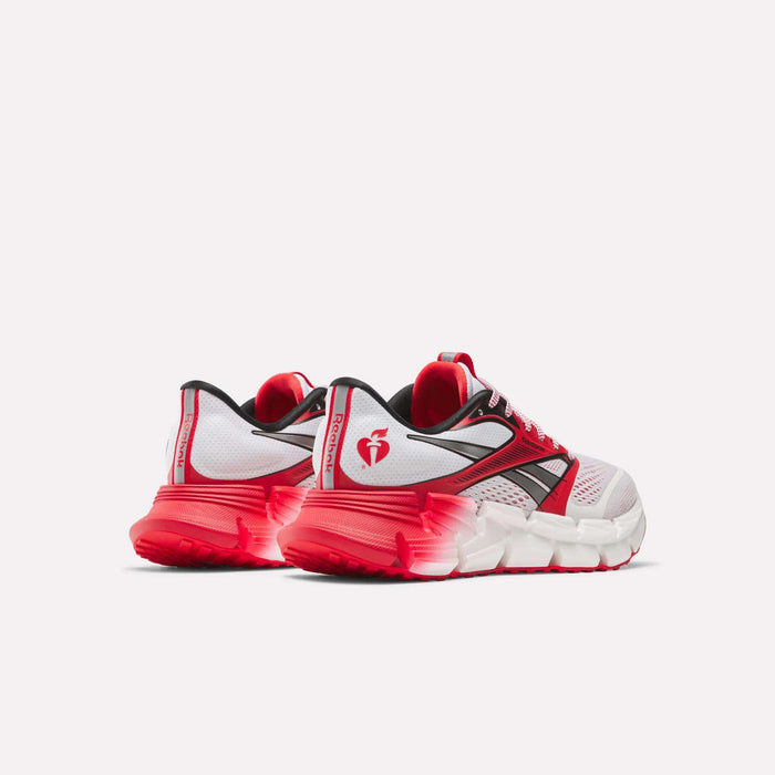 A pair of Reebok Men's FloatZig 2 AHA Running Shoes with white uppers, black and red accents, bright red soles, energy-returning cushioning, and a heart logo on the heel are shown facing away to display the back and side.