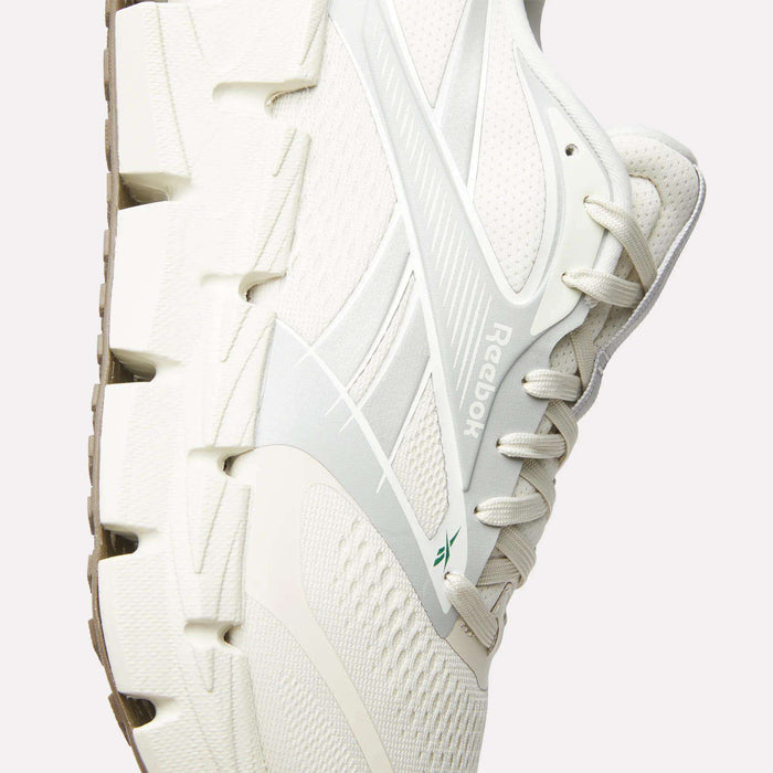 Close-up of a white Reebok Men's FloatZig 2 Running Shoe, showing mesh and synthetic details, white laces, textured sole, the visible Reebok logo on the side, and featuring Superfloat+ cushioning for enhanced comfort.