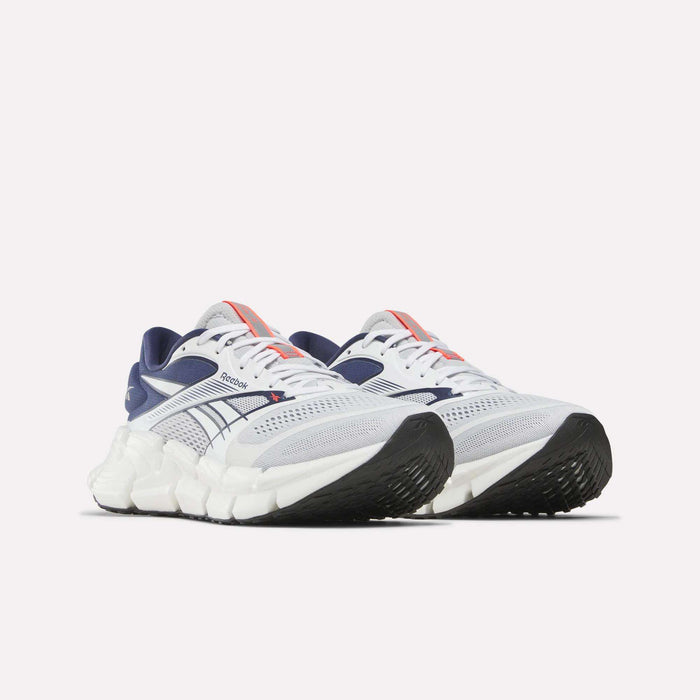 A pair of Reebok Men's FloatZig 2 Running Shoes in white with navy blue and red accents, Superfloat+ cushioning, chunky white sole, and black textured outsoles displayed against a plain white background.