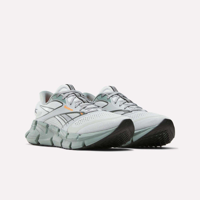 The Reebok Men's FloatZig 2 Running Shoes in white and light gray feature supportive uppers, black soles, orange accents, green detailing, and Superfloat+ cushioning, shown on a plain white background.