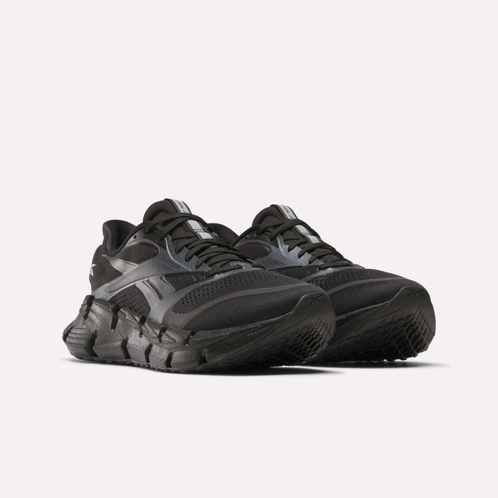 A pair of black Reebok Men's FloatZig 2 Running Shoes with thick, textured soles and mesh uppers, featuring energy-returning cushioning, are positioned side by side on a white background.