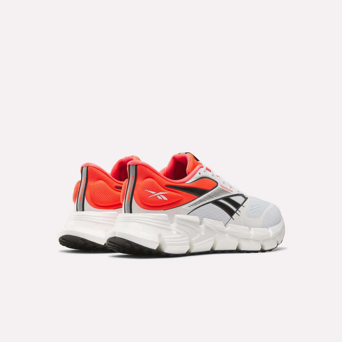 Reebok Men's FloatZig 2 Running Shoes with a chunky white sole, Superfloat+ cushioning, white mesh toe, black side stripes, grey accents, and vibrant red-orange heel and lining shown from the back and side on a plain light background.