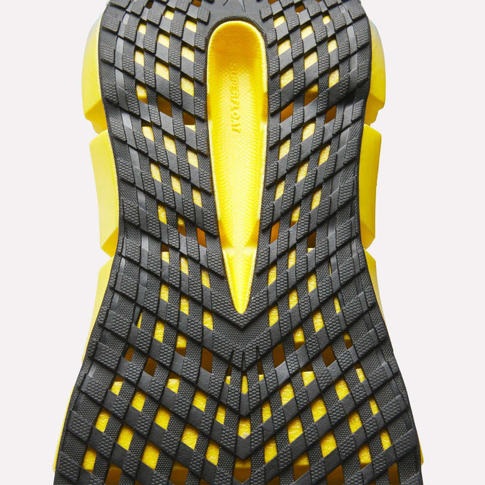 Close-up of the yellow sole of Reebok Men's FloatZig 2 Running Shoes, featuring a black grid-like rubber tread and textured design with Superfloat+ cushioning, set against a white background.