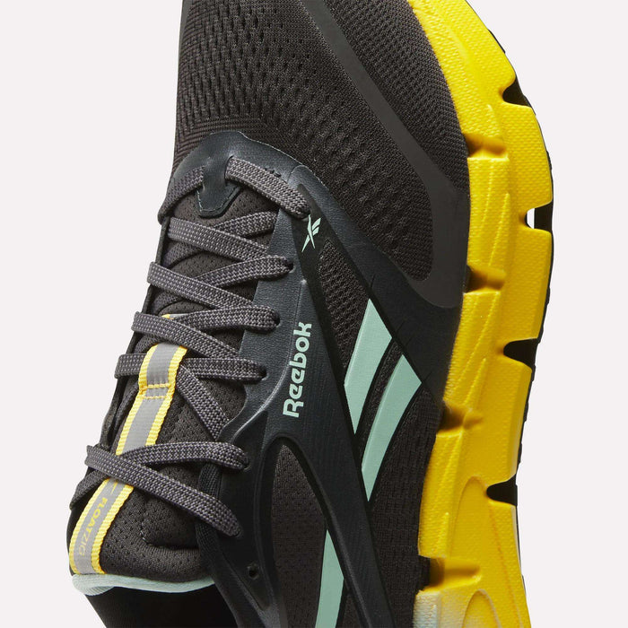 Close-up of a black Reebok Men's FloatZig 2 Running Shoe with gray laces, light blue stripes, and a thick, textured yellow sole featuring Superfloat+ cushioning. Reebok logo is visible on the side.