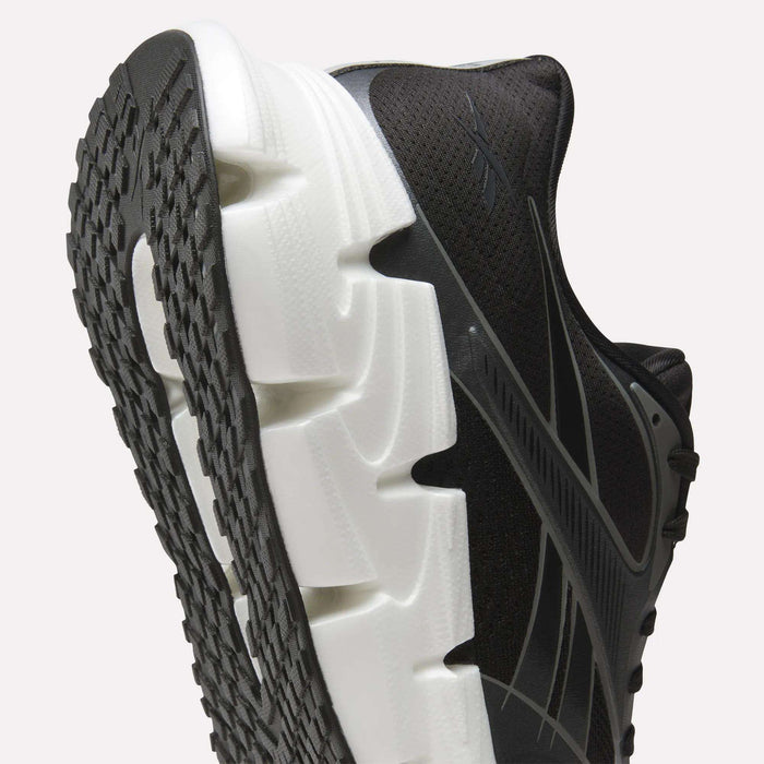 Close-up of Reebok Men's FloatZig 2 Running Shoes in black, featuring Superfloat+ cushioning, a thick white textured sole, patterned black outsole, and sleek light-colored side accents against a plain background.