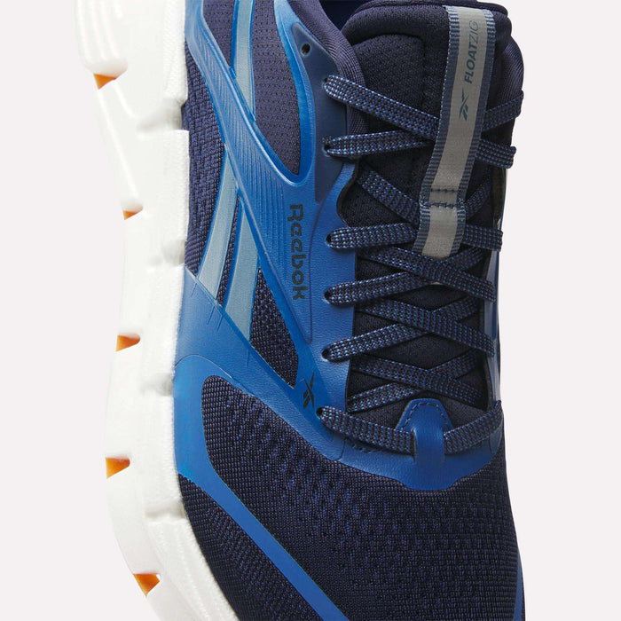Close-up of Reebok Men's FloatZig 2 Running Shoes in navy and blue, featuring Superfloat+ cushioning, a white and orange sole, mesh upper, laces, and the Reebok logo on the side and tongue.