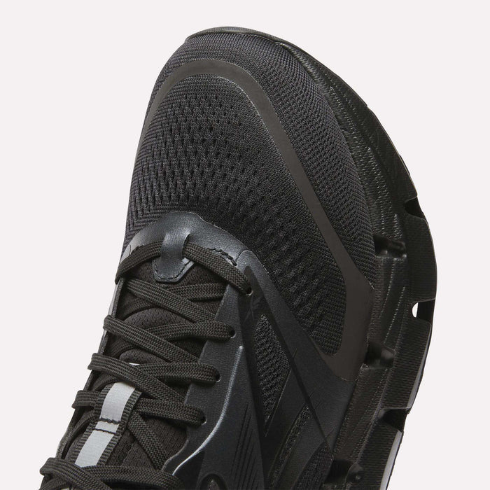 Close-up of the front and side of Reebok Men's FloatZig 2 Running Shoes in black, showing mesh fabric, laces, textured rubber sole, and energy-returning cushioning for enhanced comfort.
