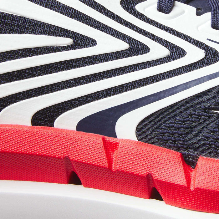 Close-up of Reebok Men's FloatZig Tread Running Shoes featuring dark blue mesh, white wavy overlays, and a textured red rubber sole with deep grooves—ideal for treadmill workouts and running.