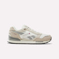 A pair of Reebok Men’s GL1600 Shoes in Elevated Beige, Linen, and Chalk is displayed on a plain white background. Featuring a low profile design inspired by the classic GL1600, these sneakers showcase side branding, a small flag detail, a durable rubber sole, and subtle suede accents for added texture and style.
