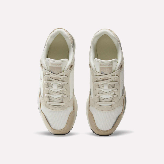 A pair of Men’s GL1600 Shoes by Reebok in cream and beige, viewed from above, showcasing the laces and the Reebok branding on the tongue of each shoe. Subtle suede accents lend a classic touch to these stylish sneakers.