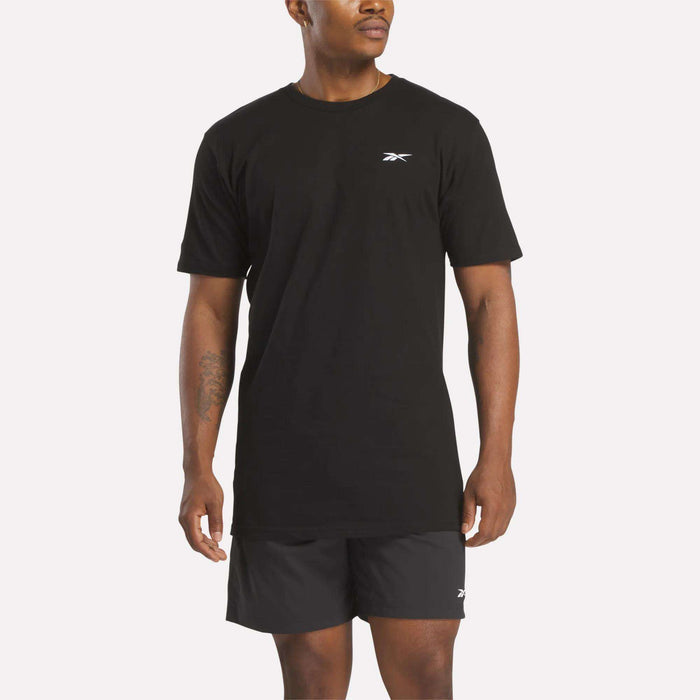A man in a relaxed fit black Reebok Men's Identity Small Logo T-Shirt and matching shorts stands against a light background, facing slightly to the side.