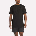 A man in a relaxed fit black Reebok Men's Identity Small Logo T-Shirt and matching shorts stands against a light background, facing slightly to the side.