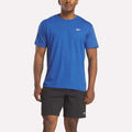 A man wears a bright blue Reebok Men's Identity Small Logo T-Shirt in a relaxed fit and black Reebok shorts, standing against a plain white background.