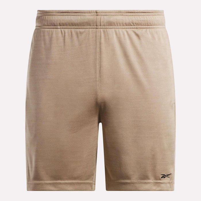 The Reebok Men's Inclination Shorts feature tan, soft fabric and an elastic waistband. A small black Reebok logo accents the lower left leg. These athletic shorts are shown against a plain, light background.