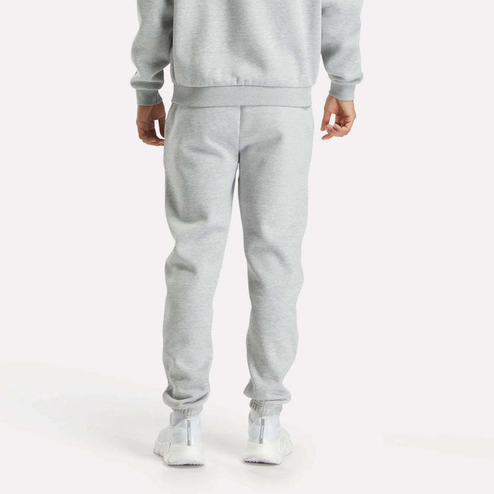 A person faces away, wearing Reebok Men's Joggers in light gray with a matching sweatshirt and white sneakers, set against a plain white background.