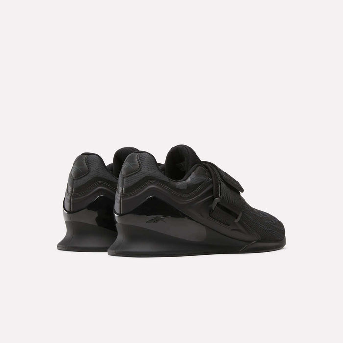 A pair of Reebok Men's Legacy Lifter IV Shoes in black features textured uppers, chunky soles, visible laces, and the Reebok logo on the heel—engineered for enhanced stability during workouts.