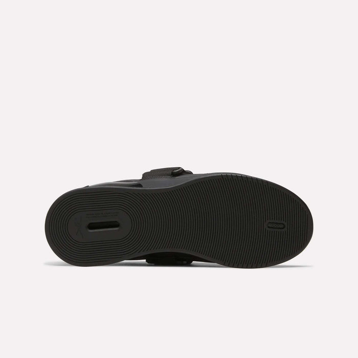 The image shows the bottom view of the Reebok Men's Legacy Lifter IV Shoes, featuring a black textured rubber sole with circular grip patterns for stability and a small rectangular cutout near the heel.