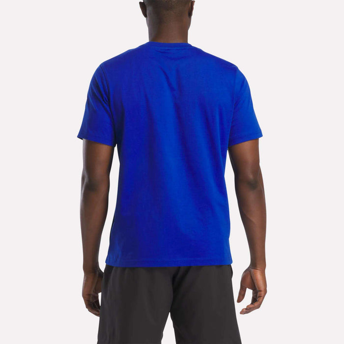 A person stands with their back to the camera, wearing a bright blue Reebok Men's Logo Crewneck T-Shirt and black shorts, set against a plain white background.