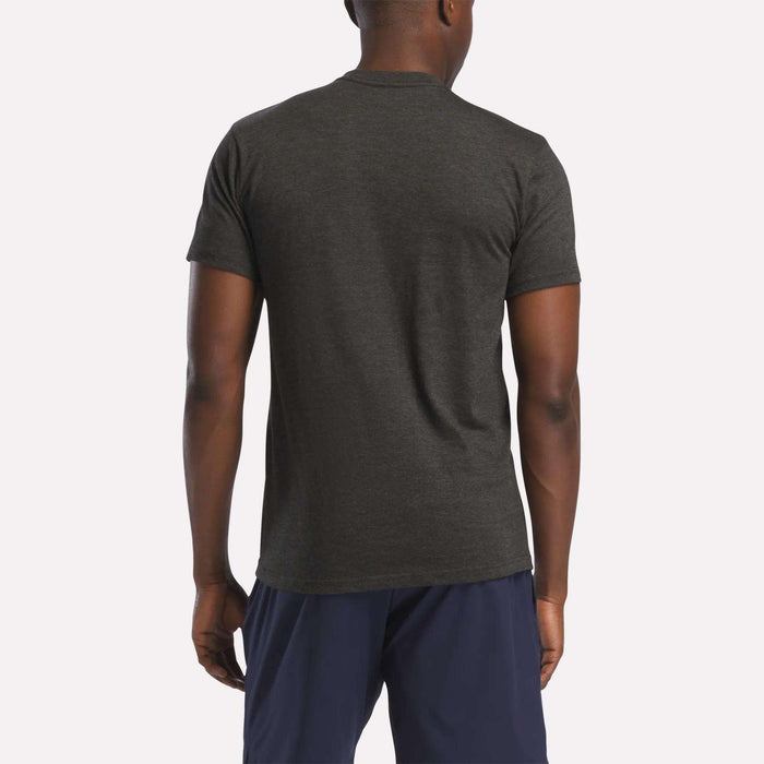 A person wearing a dark gray Reebok Men's Stacked Vector Graphic T-Shirt and navy blue shorts stands with their back to the camera against a plain, light background.