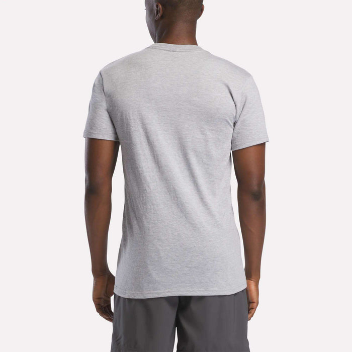 A man, back to the camera, wears a light gray Reebok Men's Stacked Vector Graphic T-Shirt made from lightweight 100% cotton with dark gray shorts, set against a plain light background.