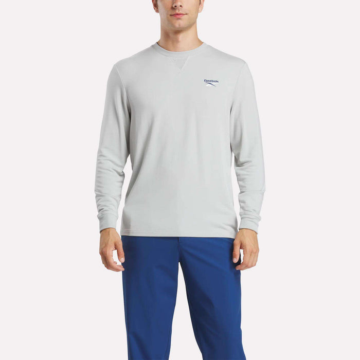 A man wears a Reebok Men's Long Sleeve Golf Sweatshirt with UPF 30+ protection, paired with blue pants.