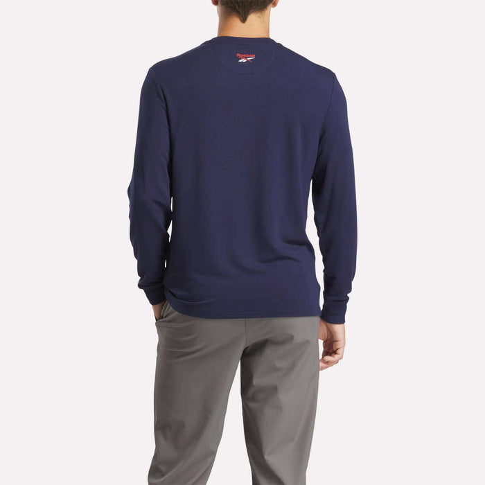 A person faces away from the camera, wearing a Reebok Men's Long Sleeve Golf Sweatshirt in navy with UPF 30+ and light gray pants, posed against a plain, light background.