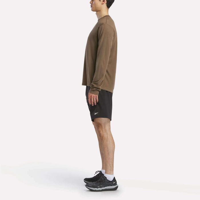 A person in profile wears a Reebok Men's Long Sleeve Tech T-Shirt, black shorts, white socks, and black running shoes against a plain white backdrop—ideal for cold weather workouts.