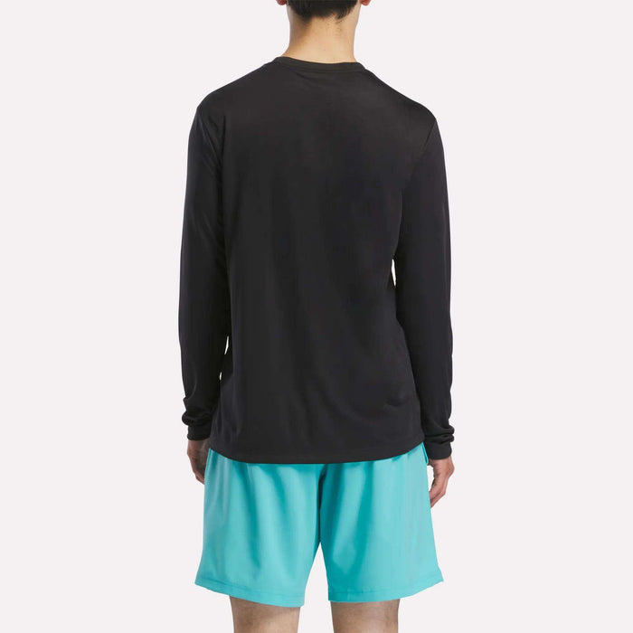A man stands with his back to the camera in a Reebok Men’s Long Sleeve Tech T-Shirt and light blue shorts, ready for cold weather workouts against a plain white background.