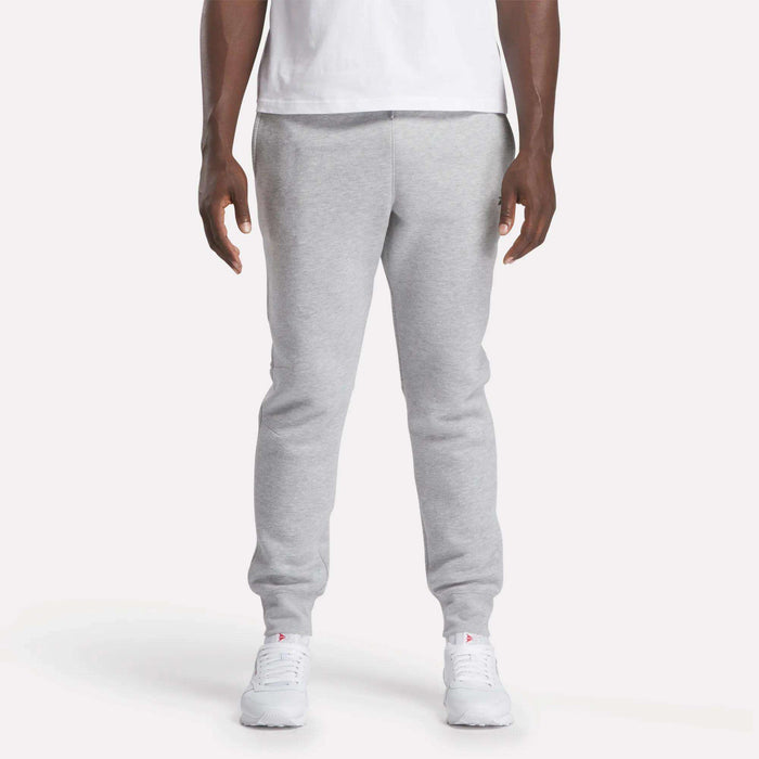 A person stands facing forward against a plain white background, wearing a white t-shirt, Reebok Men's Motion Joggers in a slim fit, and white sneakers.