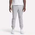 A person stands facing forward against a plain white background, wearing a white t-shirt, Reebok Men's Motion Joggers in a slim fit, and white sneakers.