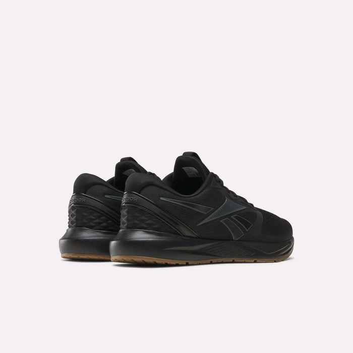 The Reebok Men's Nanoflex Trainer 2 Shoes, shown in black with dark gray accents, feature textured heels and brown outsoles, displayed from a rear side angle against a light background.