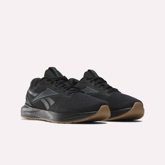 The Reebok Men's Nanoflex Trainer 2 Shoes are black with gray accents and a brown rubber sole, shown on a white background. They feature a mesh upper and the Reebok logo on the side, making them ideal for workouts.