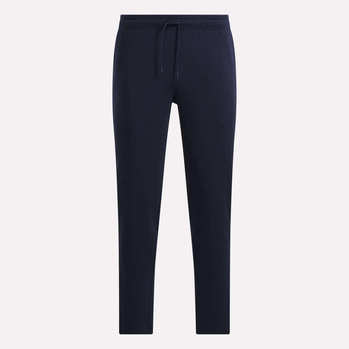 Reebok Men’s Patent Pant in navy blue, made from soft knit fabric, features an elastic waistband with drawstring and tapered legs, shown against a plain light background.