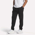 A person wearing a white t-shirt, Reebok Men's Patent Pants with an adjustable waistband, and white sneakers stands with hands in pockets against a plain white background.