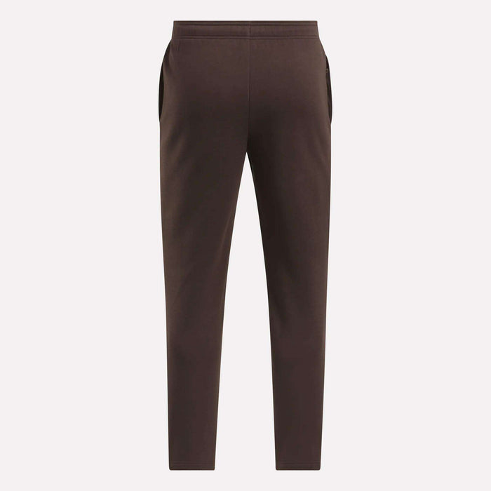 The Reebok Men's Patent Pants in brown are shown flat from the back on a light background, featuring an elastic waistband and side pockets. Made with a cotton-poly blend for comfort and durability.