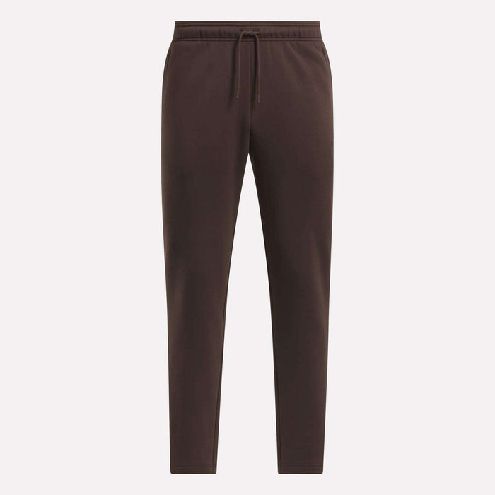 The Men's Patent Pants by Reebok are dark brown, slim fit joggers with an elastic waistband, drawstring, and tapered legs. Made from a soft cotton-poly blend, they are shown against a light background.