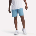 A person wearing a white shirt, Reebok Men's Range Shorts 9" in Warped Blue, and white sneakers stands against a plain white background.
