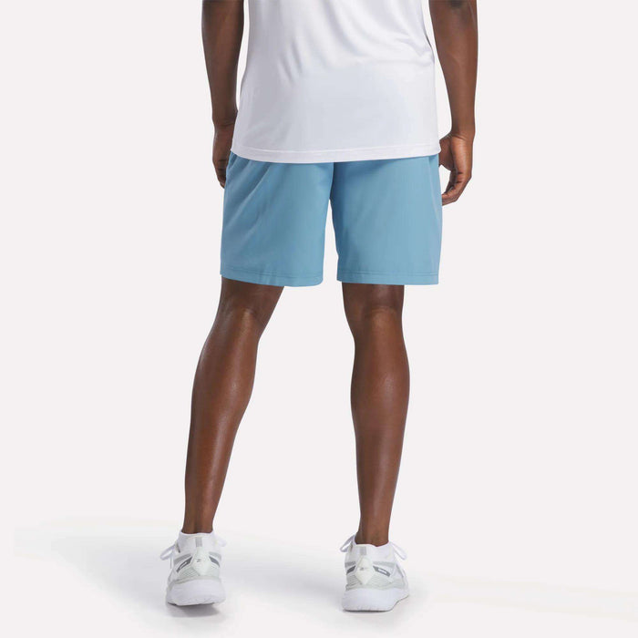 A person wearing a white shirt, Men's Range Shorts 9" from Reebok in light blue, and white sneakers stands facing away from the camera, displaying the back of their outfit against a plain white background.