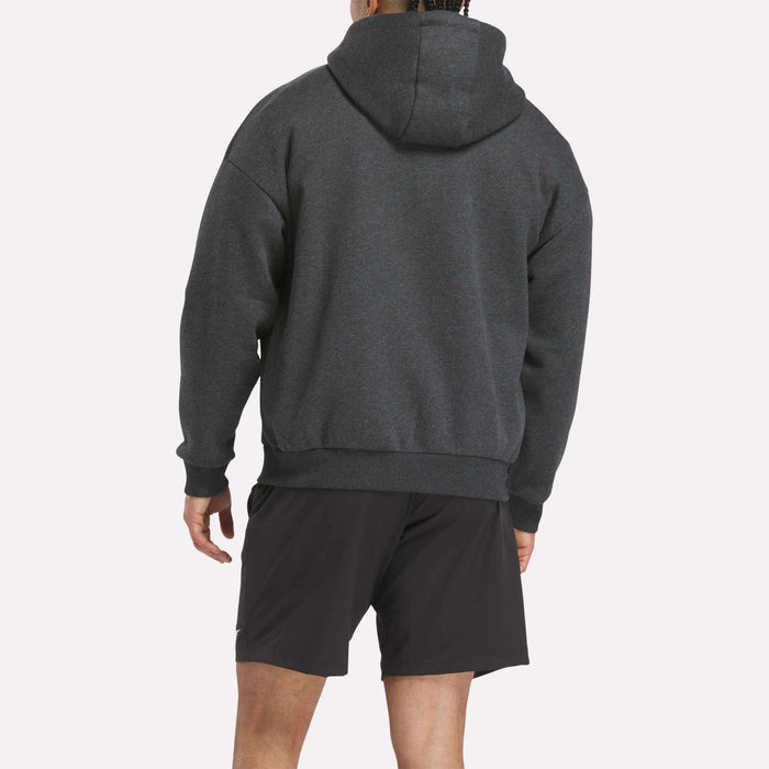 A person stands facing away from the camera, wearing a Reebok Men's Reebok x F45 Training Relaxed Hoodie and black shorts against a plain light background.