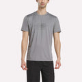 A man wears the Reebok Men's Reebok x F45 Training T-Shirt in Grey 3, featuring performance design and "RS TRAINING" print on the front, paired with black pants and standing against a plain white background.