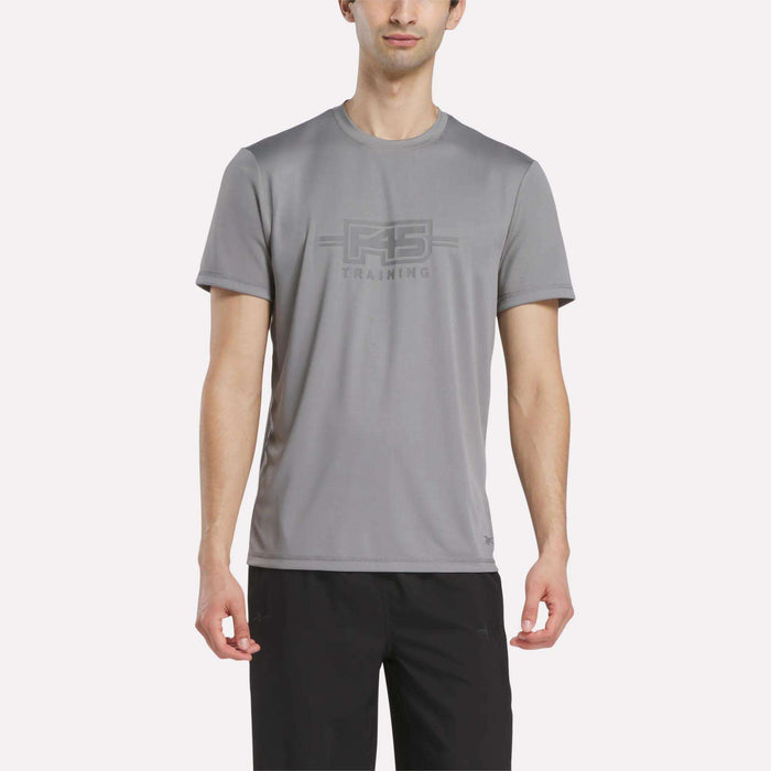 A man wears the Reebok Men's Reebok x F45 Training T-Shirt in Grey 3, featuring performance design and "RS TRAINING" print on the front, paired with black pants and standing against a plain white background.