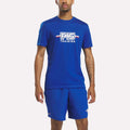 A person stands against a plain white background wearing the Men’s Reebok x F45 Training T-Shirt in Vector Blue, their arms relaxed at their sides. The comfortable Reebok apparel is designed for active lifestyles.