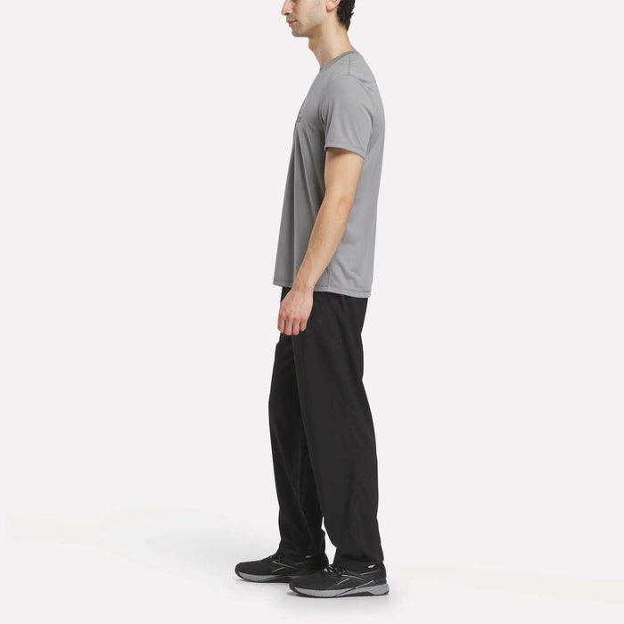 A person stands in profile, wearing the Men's Reebok x F45 Training T-Shirt and black pants with black athletic shoes, set against a plain white background—a look that’s perfect for F45 Training or any workout routine.