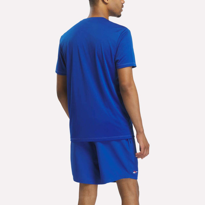 A man stands facing away, wearing a matching royal blue Reebok x F45 Training T-Shirt and shorts. The background is plain white.