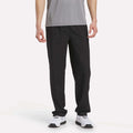 A person wearing a gray short-sleeve shirt, Men's Reebok x F45 Training Woven Pants in Vector Navy, and white athletic shoes stands against a plain white background. Their outfit is ideal for high-intensity training or F45 Training sessions, with the Reebok pants providing reliable comfort and support. Their face is not visible.