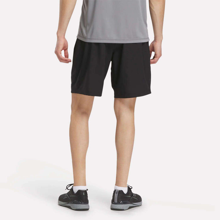 A person dressed in a gray shirt, white socks, black sneakers, and Men's Reebok x F45 Training Woven Shorts is standing with their back to the camera against a plain white background, ready for some high-intensity training.