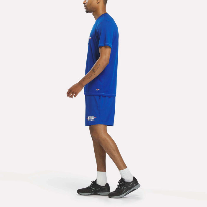 A person in a blue T-shirt and Men's Reebok x F45 Training Woven Shorts by Reebok stands sideways, wearing white socks and black sneakers against a plain white background.